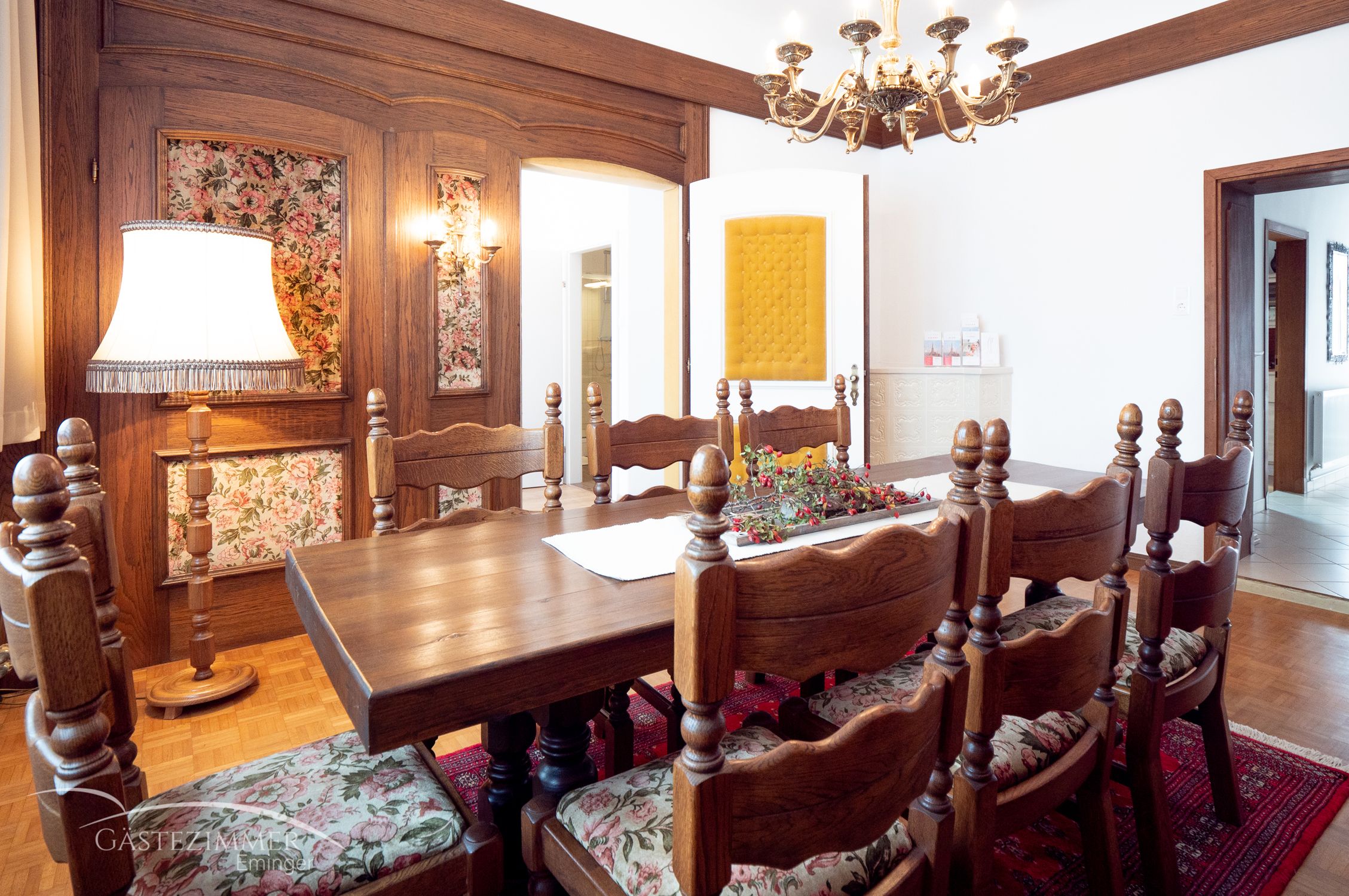 Rustic dining room with wooden furniture, chandelier and floral patterns.