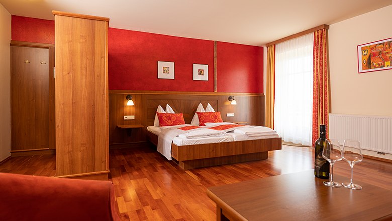Cozy hotel room with double bed, wooden furniture and red accents.