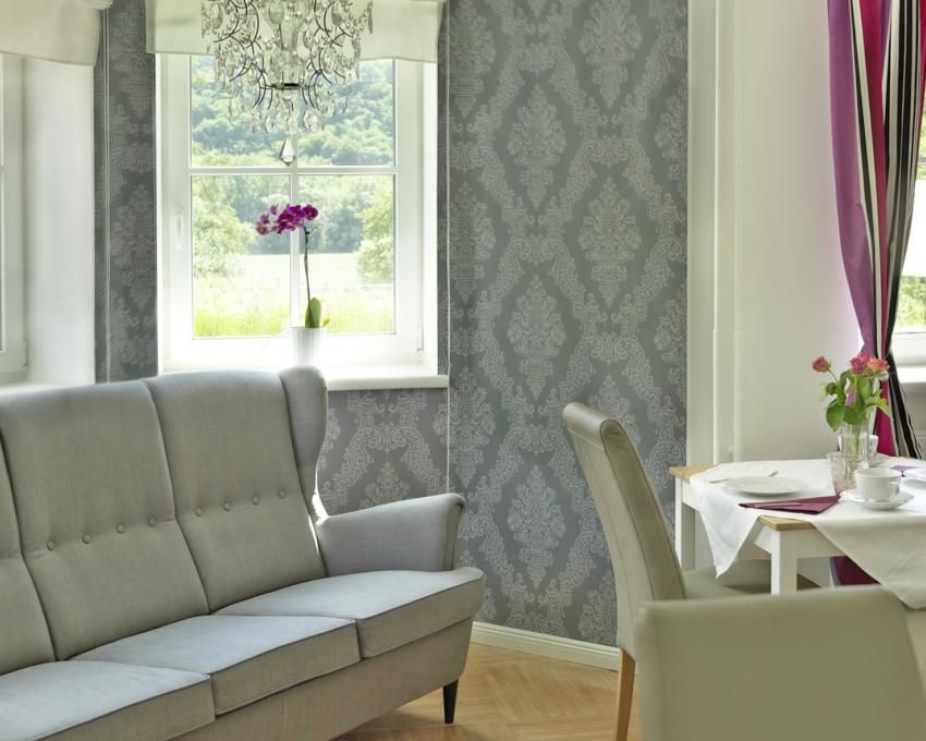 Interior of a stylish living room with gray sofa, decorative wallpaper, chandelier and dining table with flowers.