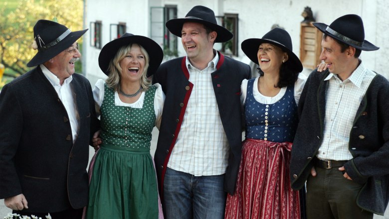 Group of five people in traditional Bavarian costume, laughing happily.