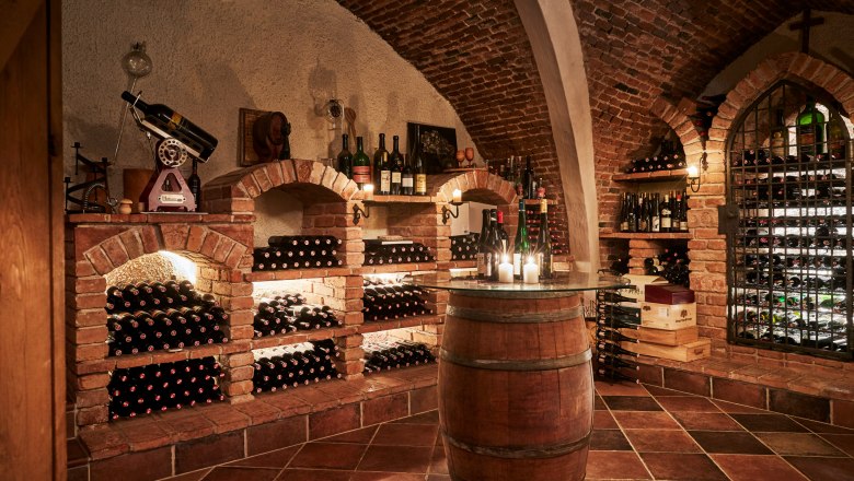 Historic wine cellar with brick vaults, wine bottles on shelves and candles on a barrel.