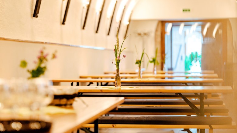 Interior view of a Buschenschank (typical tavern) with long wooden tables and benches, decorated with flower vases.