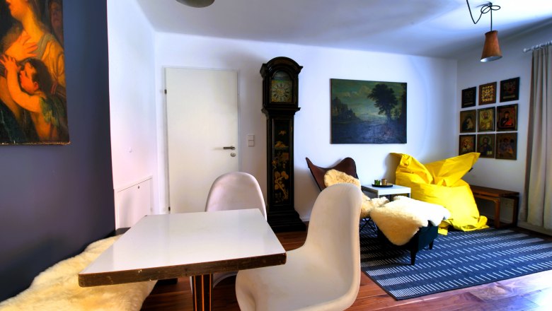 Living room with table, chairs, grandfather clock, paintings and yellow beanbag.