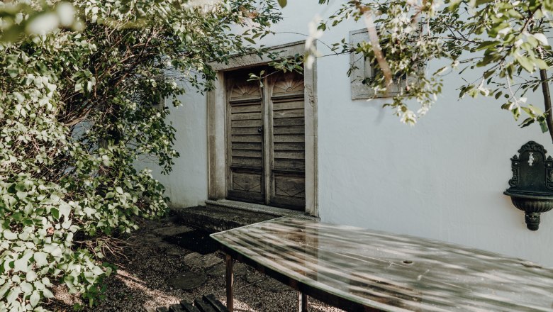 Wooden door behind trees with table in the foreground.