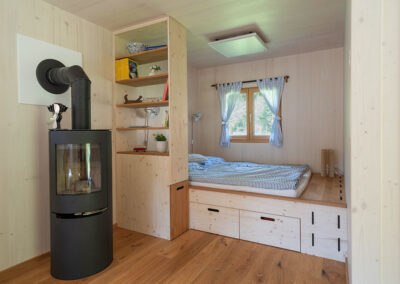 Interior view of a modular house with wood stove, shelf and bed.