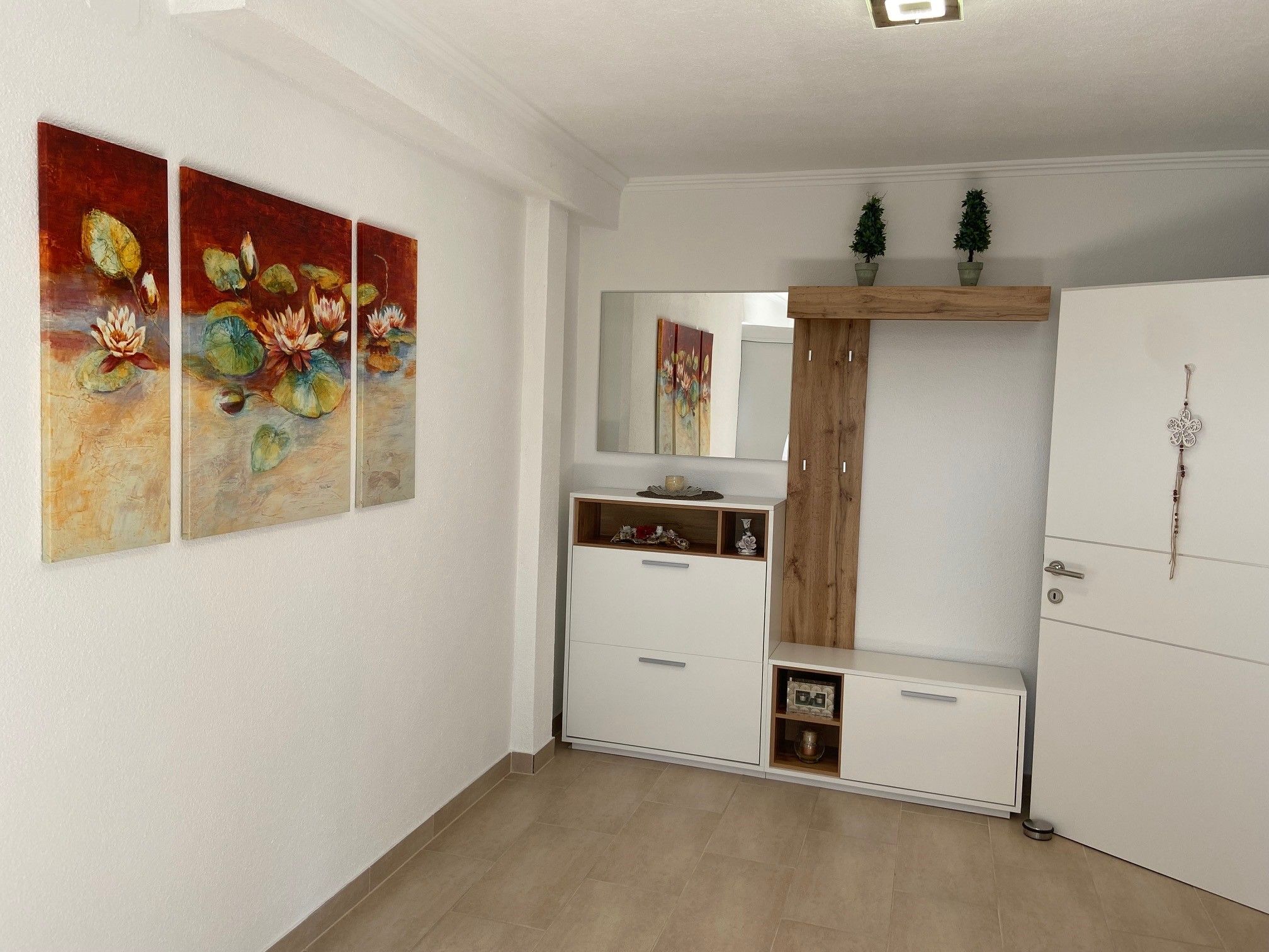 An anteroom with a three-part water lily picture on the wall, a white cabinet with mirror and decorations.
