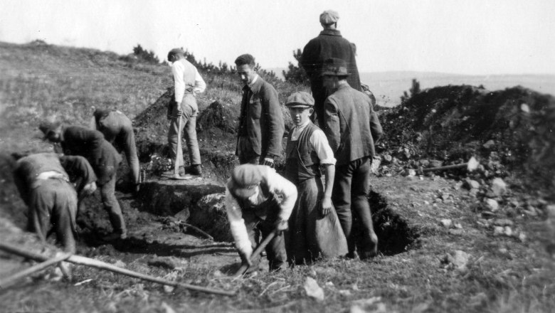 Black and white photo of men digging in a field.
