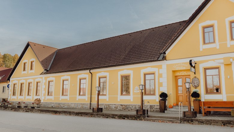 Yellow pub with a brown roof and several windows, decorated with pumpkins in front of the entrance.