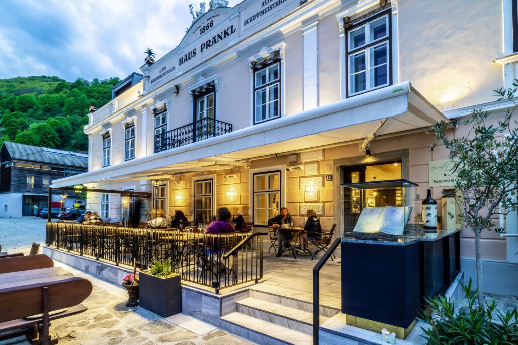 Exterior view of Gasthof Prankl with illuminated terrace and guests at tables.