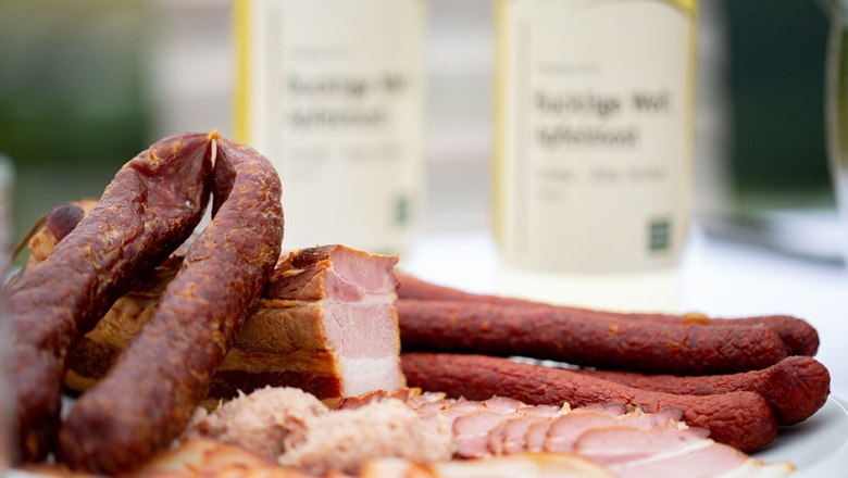 Close-up of sausage and meat specialties on a plate with bottles in the background.