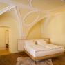 An elegant bedroom with a vaulted ceiling, a double bed, an armchair and wooden floor.