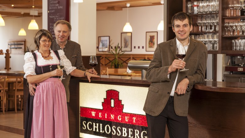 Three people stand at a bar in the Schlossberg winery with glasses of wine in their hands.