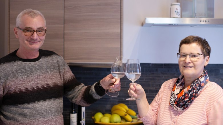 Two people clink glasses of wine in a kitchen.