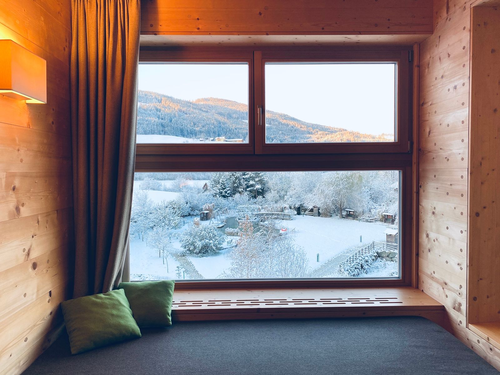View from a wooden window of a snowy landscape with mountains in the background.