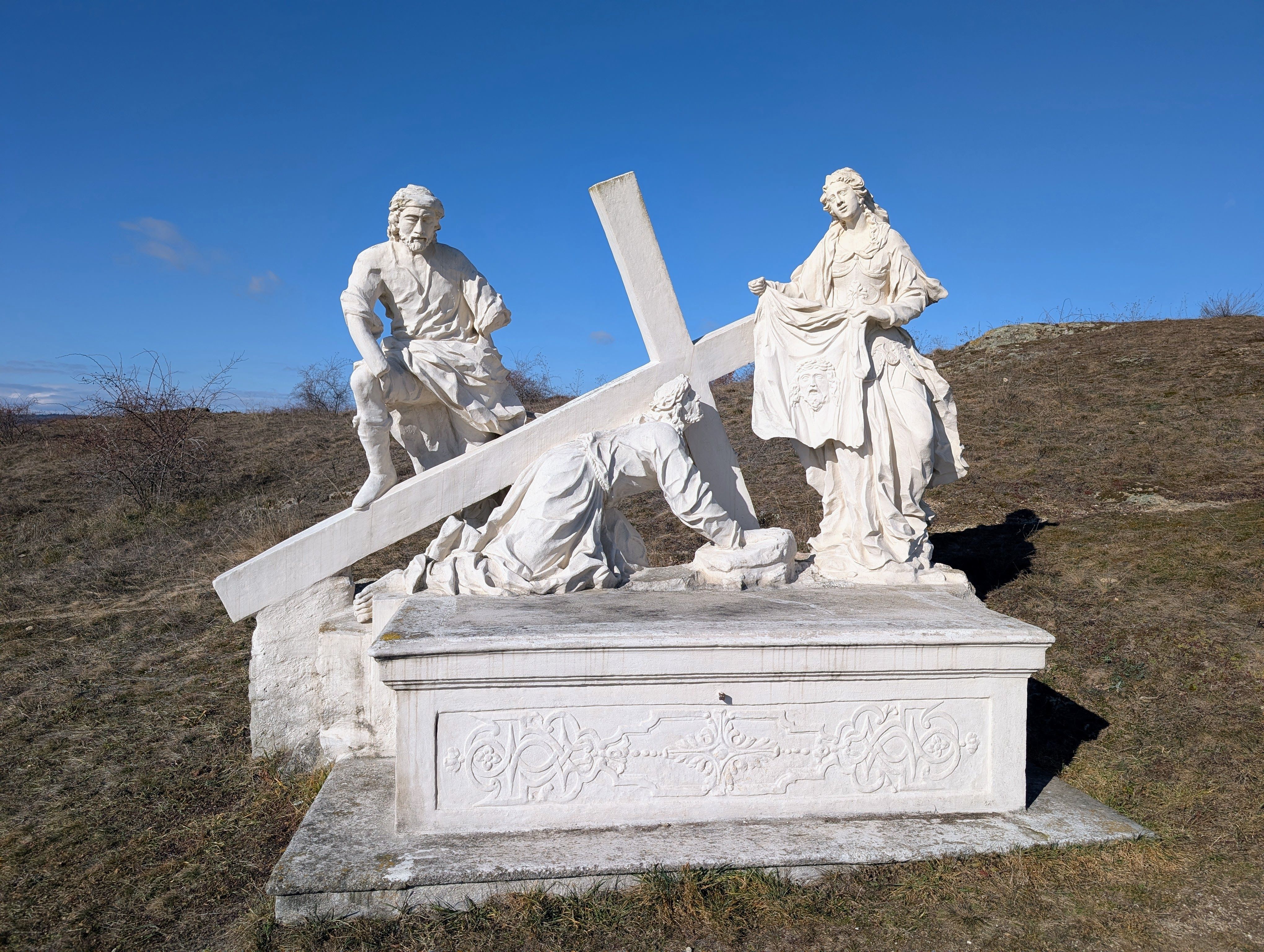 Stone sculpture of a religious scene with three figures and a cross on a hill.