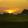 Sunset over a golf course with flag and small building.