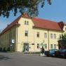 Exterior view of a yellow building with a red roof, Junges Hotel Tulln, surrounded by trees and parked cars.
