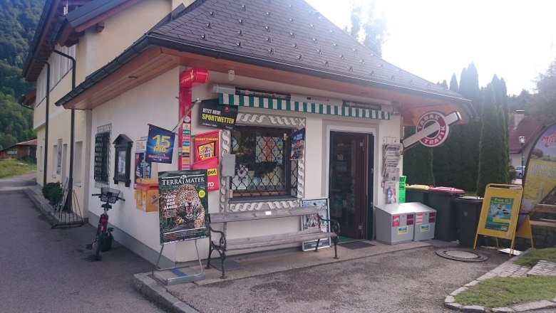 Exterior view of a small tobacco store with advertising signs and newspaper stands.