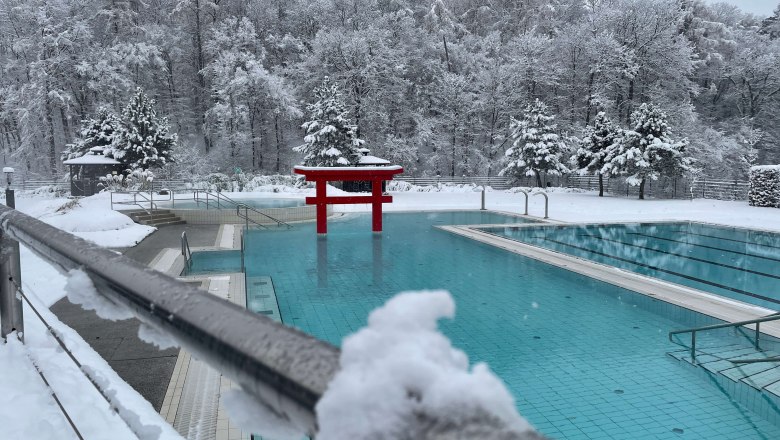A snow-covered outdoor pool at a thermal spa with red Asian elements and snow-covered trees in the background.