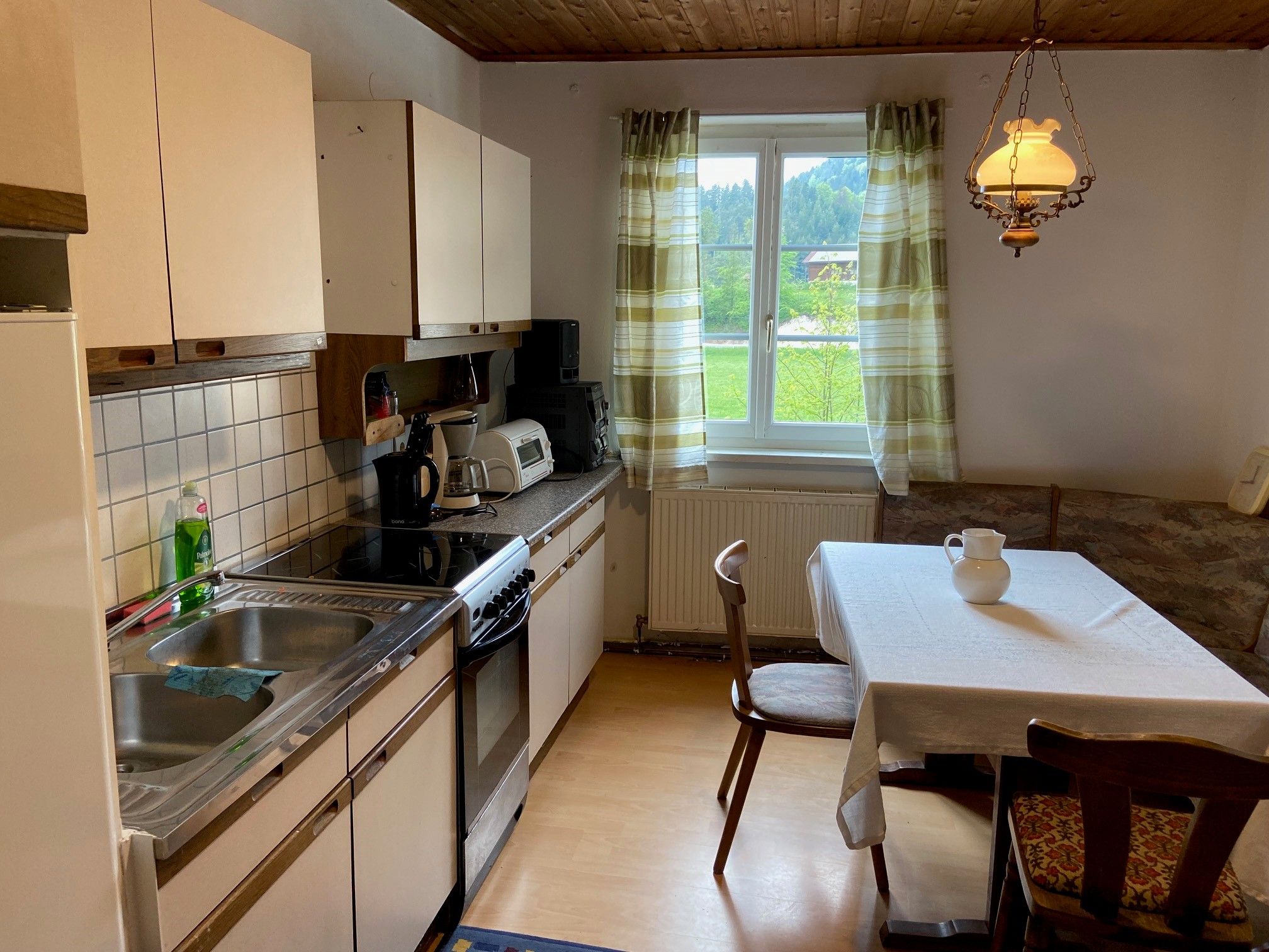 Kitchen with dining table, chairs, sink, stove and window with curtains.