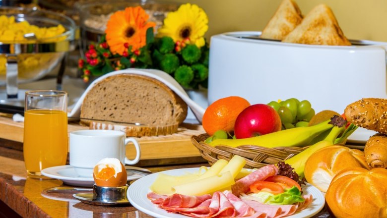 Breakfast buffet with bread, cold cuts, cheese, fruit, rolls, juice and egg.