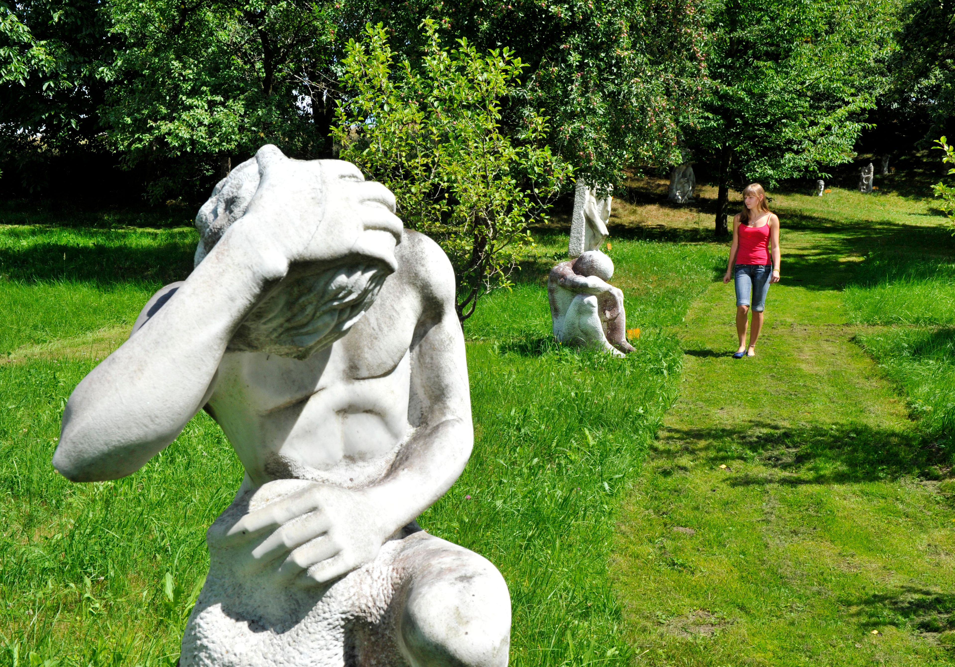 A woman walks through a garden with several sculptures on a green meadow.