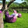 A garden with purple beanbags and a table on a green lawn, surrounded by a wooden fence and trees.