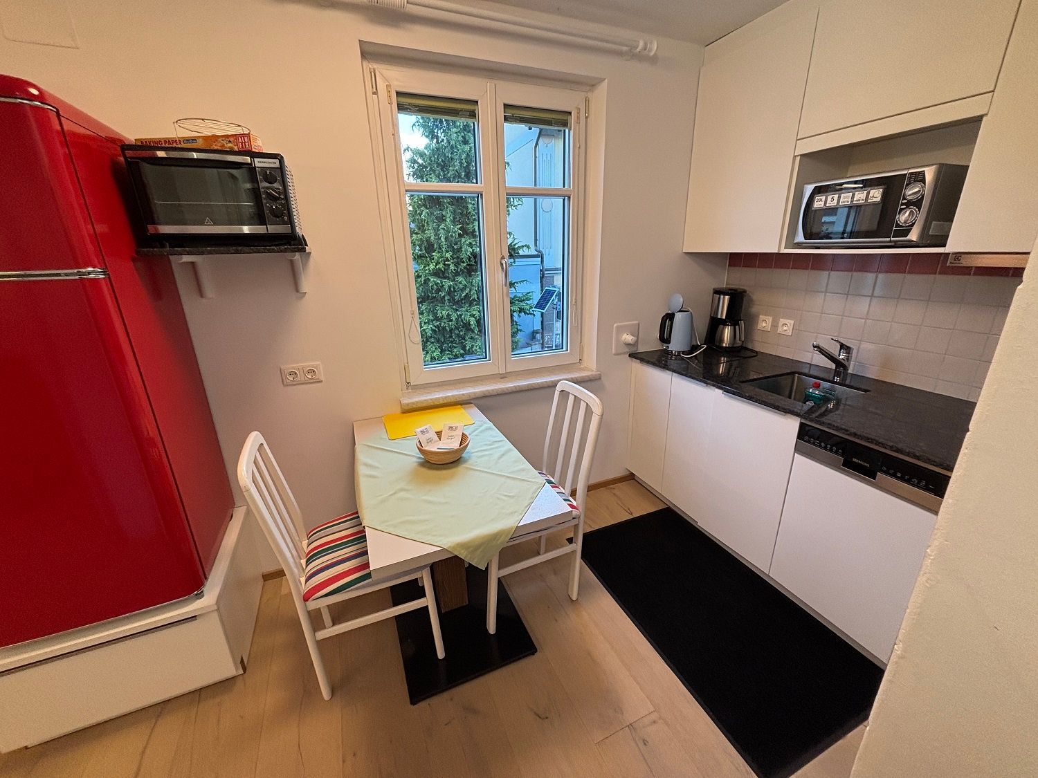 Small kitchen with red fridge, table, chairs and kitchenette.