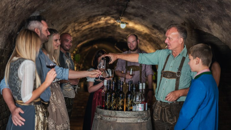 A group of people in traditional dress at a wine tasting in a wine cellar.