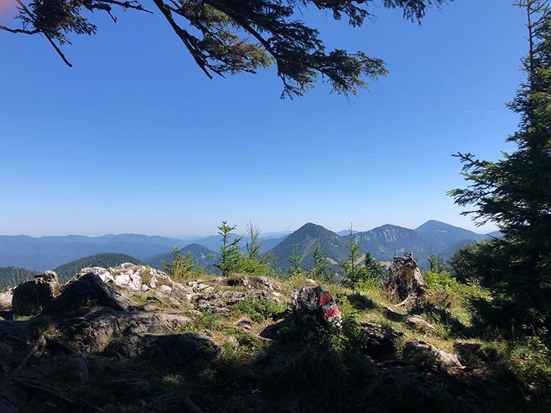 Mountain landscape with rocks and trees in the foreground, blue sky in the background.