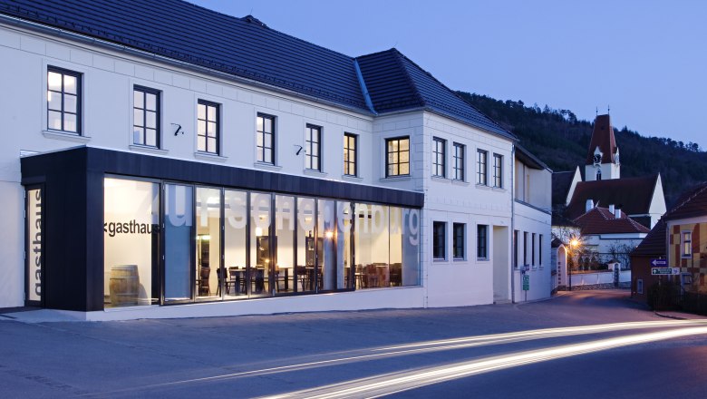Exterior view of the Gasthof Hotel Zur Schonenburg at dusk with illuminated windows and passing cars.