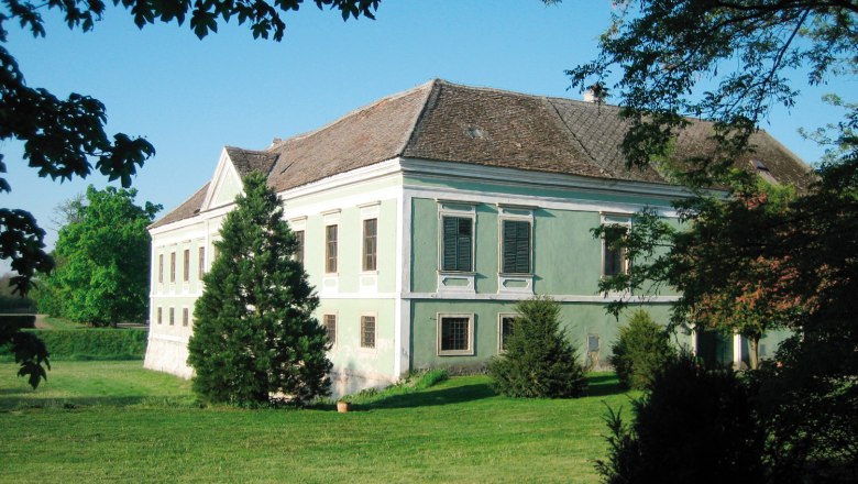 An old castle with green paint and a tiled roof, surrounded by trees and lawns.