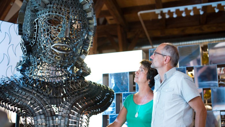 Two people look at a large metal sculpture in an exhibition.
