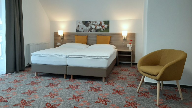 Modern double room with two beds, yellow cushions, carpet with floral pattern and a yellow armchair.
