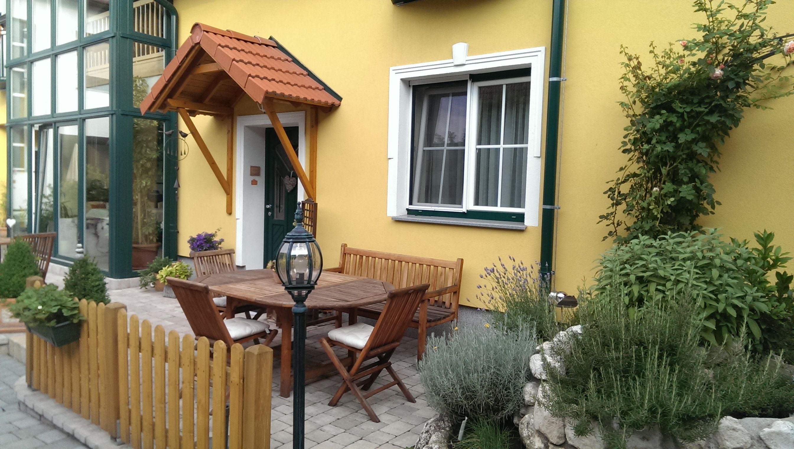 A cozy courtyard with wooden furniture, plants and a yellow façade.