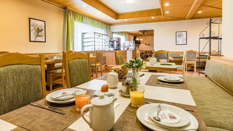 A cozy breakfast room with laid tables, juice glasses and coffee pots.
