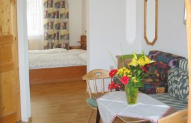 A cozy room with wooden furniture, a bed in the background and a table with flowers in the foreground.