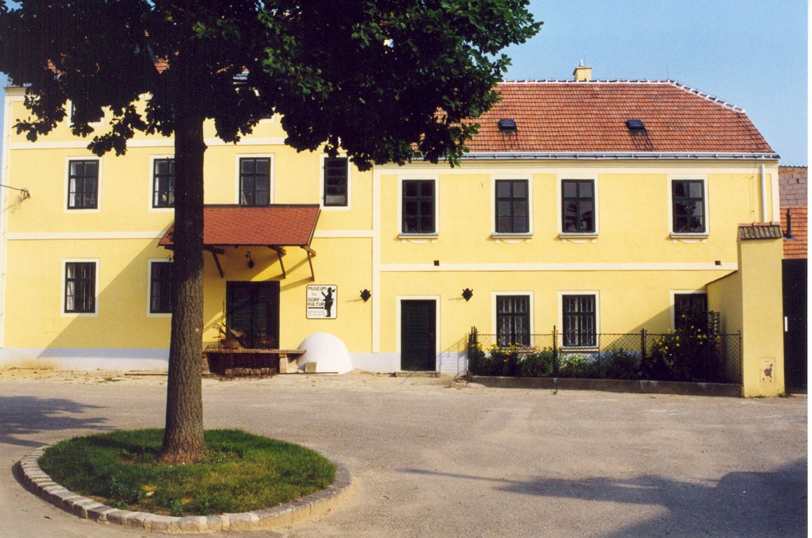 Yellow building with red roof and tree in the foreground.