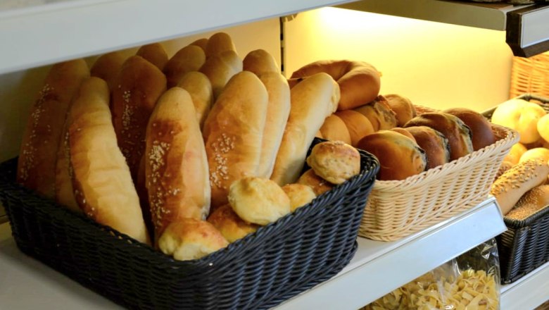 Shelf with various types of bread in baskets, including baguettes and rolls.