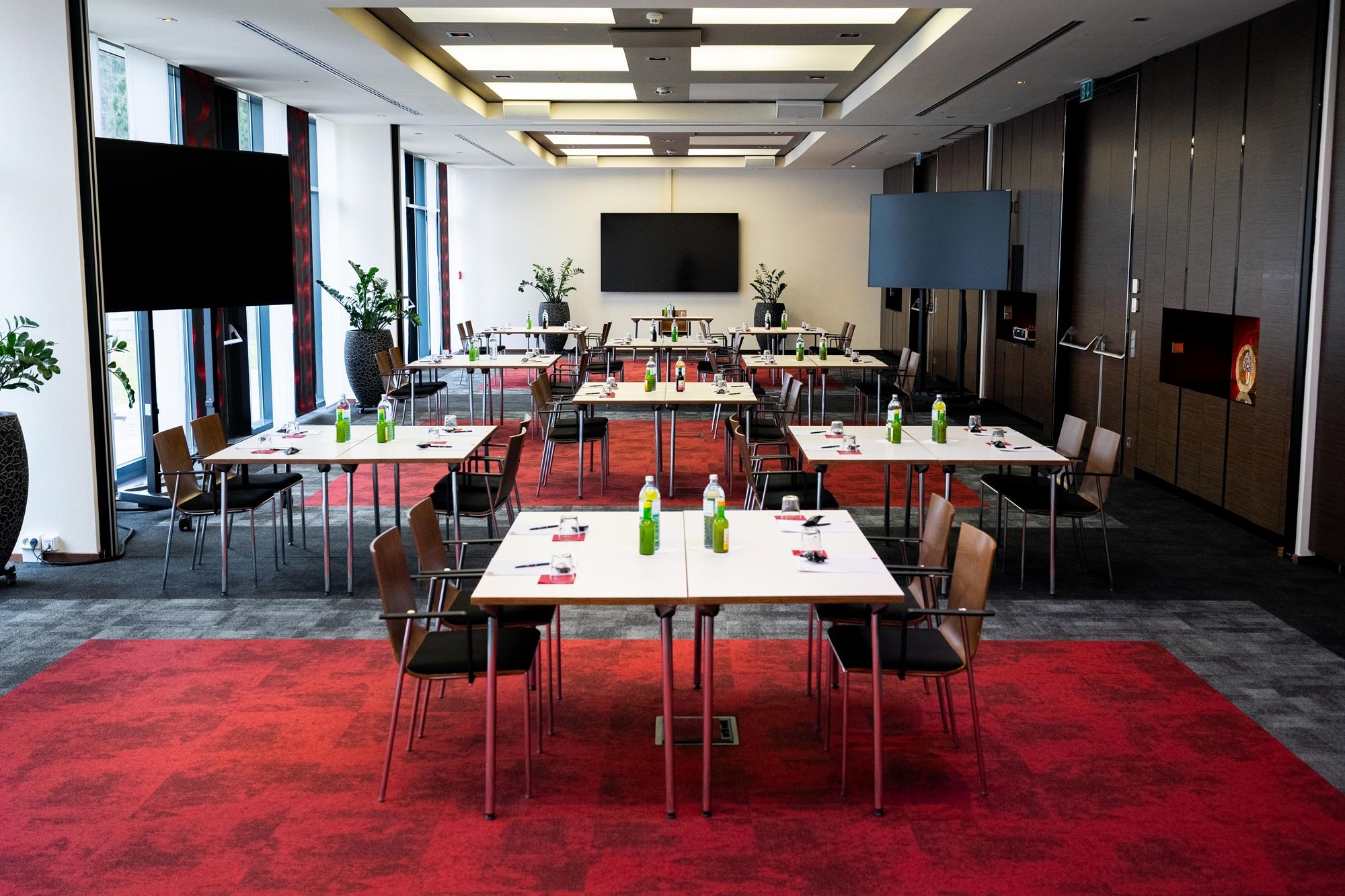 A modern conference room with red carpets, white tables and chairs, equipped with beverages and writing supplies.