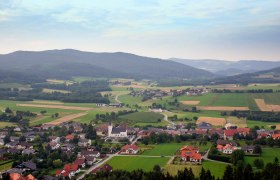 Landscape view of M&uuml;nichreith am Ostrong with fields, houses and hills in the background.