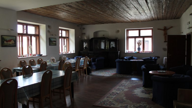 SOLA Safov, © Hannes Messmann A cozy room with wooden tables, chairs and sofas, decorated with carpets and pictures on the walls.