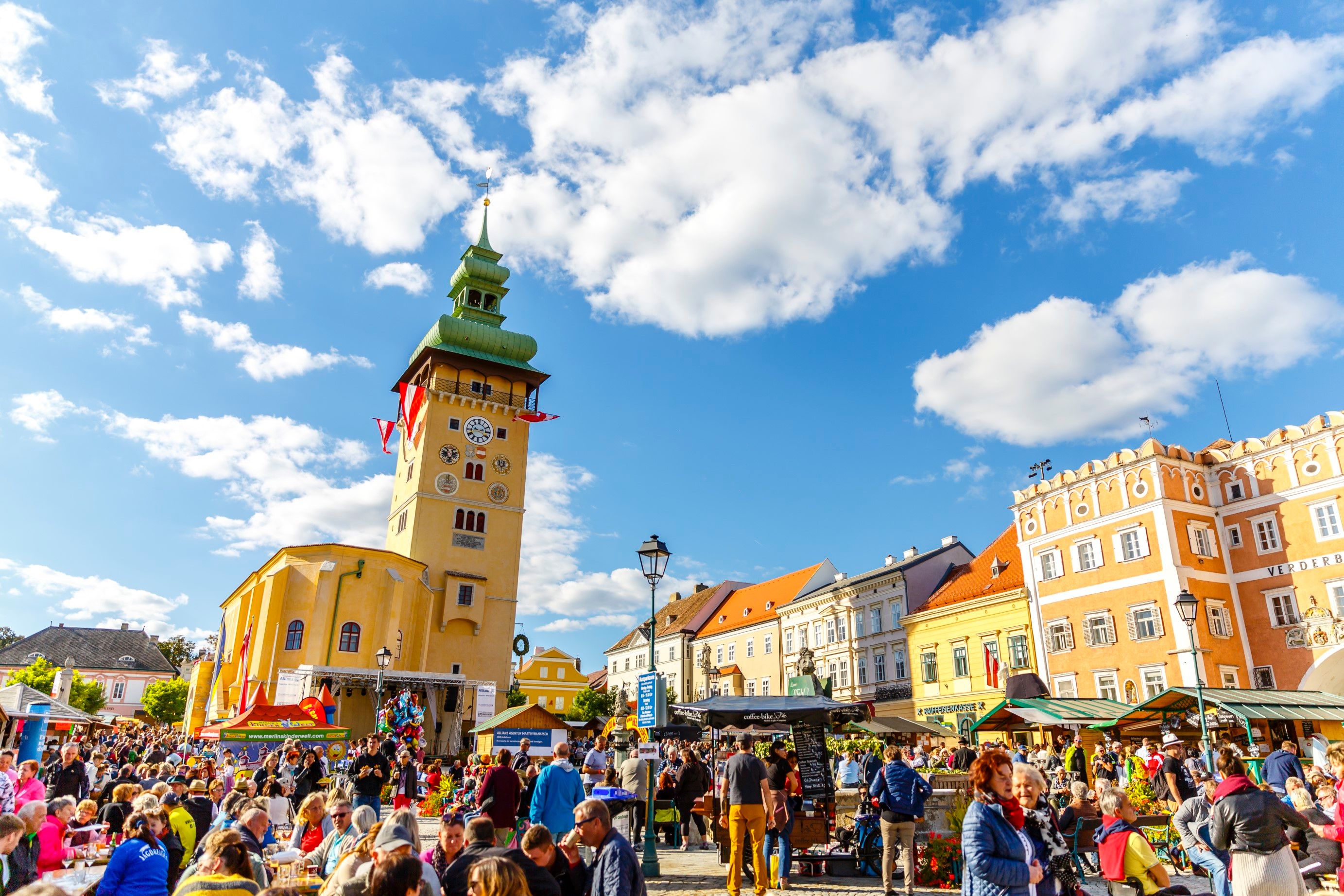 Crowd on a busy square in Retz with a striking clock tower in the background.