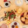 A laid breakfast table with bread rolls, cold cuts, jam, coffee, orange juice and a bouquet of flowers in the middle.