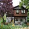 A two-story wooden house with flower boxes and garden.