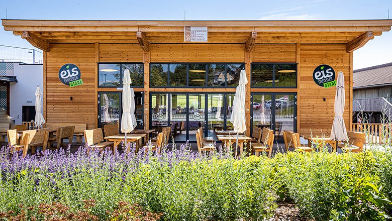 Modern wooden building with terrace with benches, chairs and parasols.