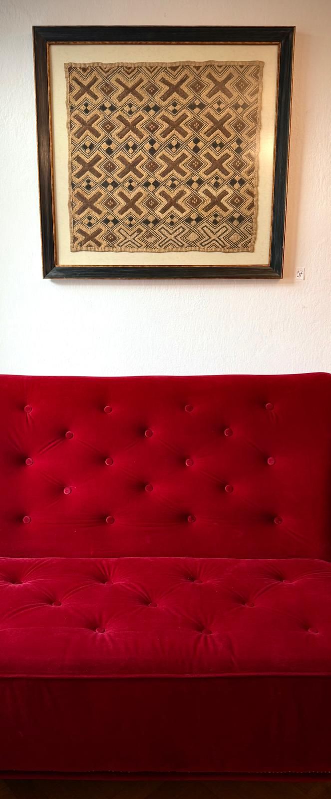 Red sofa in front of a framed, patterned work of art on the wall.