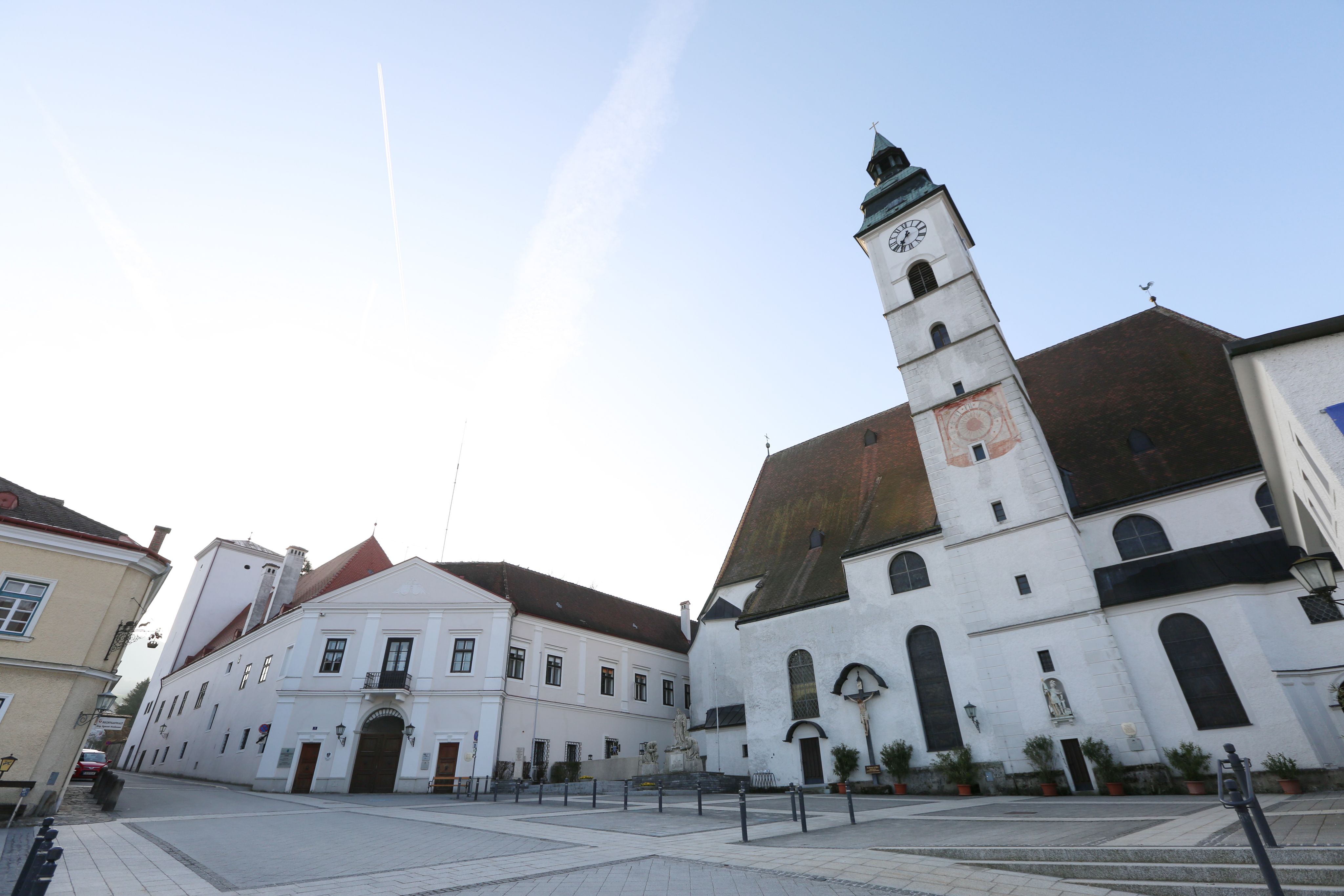 Parish church with clock tower and adjoining buildings on an empty square.