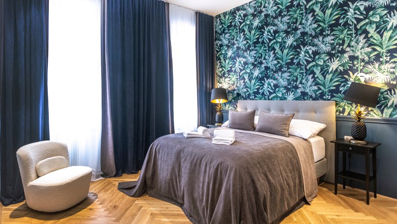 Modern double room with gray bed, tropical wallpaper and dark curtains.