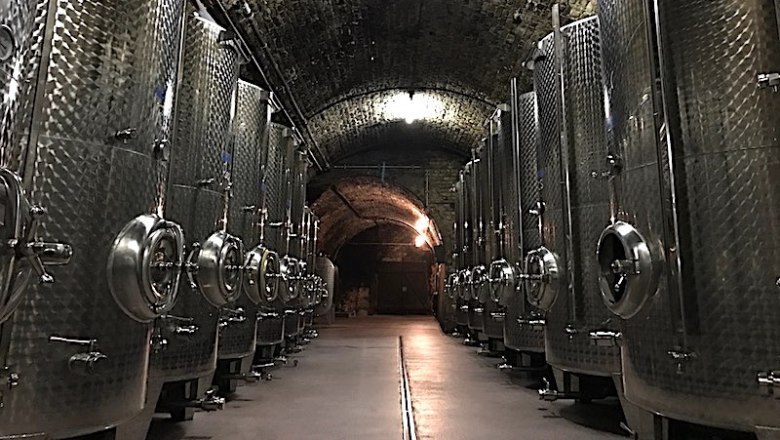 A wine cellar with large stainless steel tanks in a vaulted, stone room.